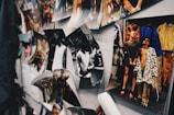 A collection of photographs is displayed on a wall, including both black and white and color images. One image shows a group of people in stylish and bold clothing, while another displays an individual in a casual pose. The arrangement appears informal, with some photos curling at the edges.