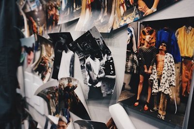 A collection of photographs is displayed on a wall, including both black and white and color images. One image shows a group of people in stylish and bold clothing, while another displays an individual in a casual pose. The arrangement appears informal, with some photos curling at the edges.