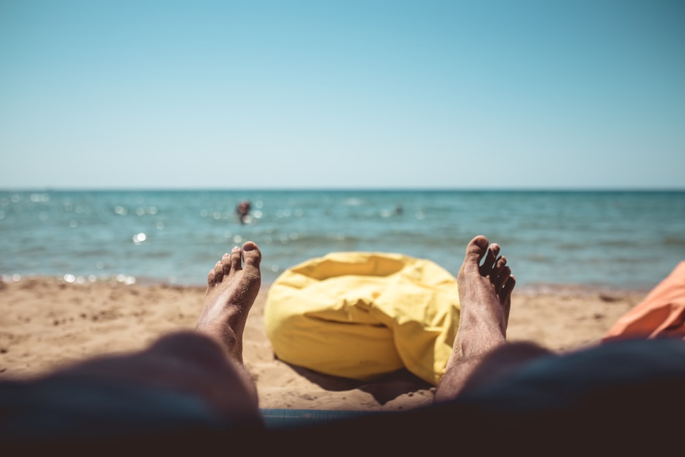lying person on sand beside yellow bean bag during daytime