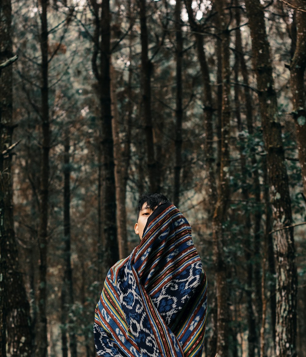boy with shawl standing between forest