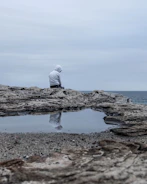 a man sitting on cliff overlooking a gloomy sea