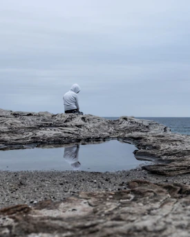a man sitting on cliff overlooking a gloomy sea