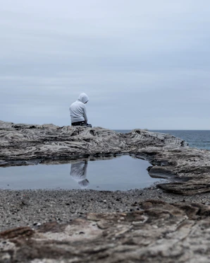a man sitting on cliff overlooking a gloomy sea