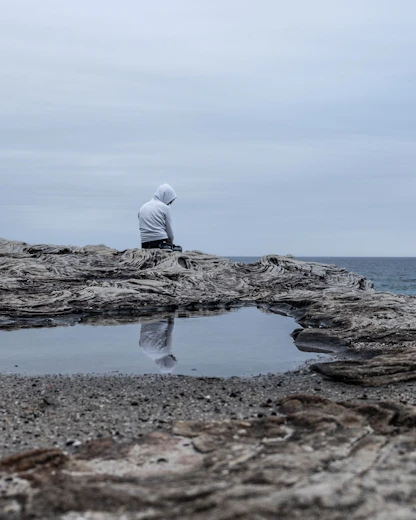 a man sitting on cliff overlooking a gloomy sea