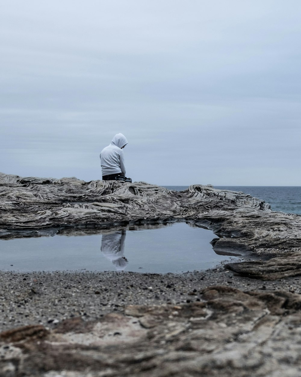 Ein Mann sitzt auf einer Klippe mit Blick auf ein düsteres Meer