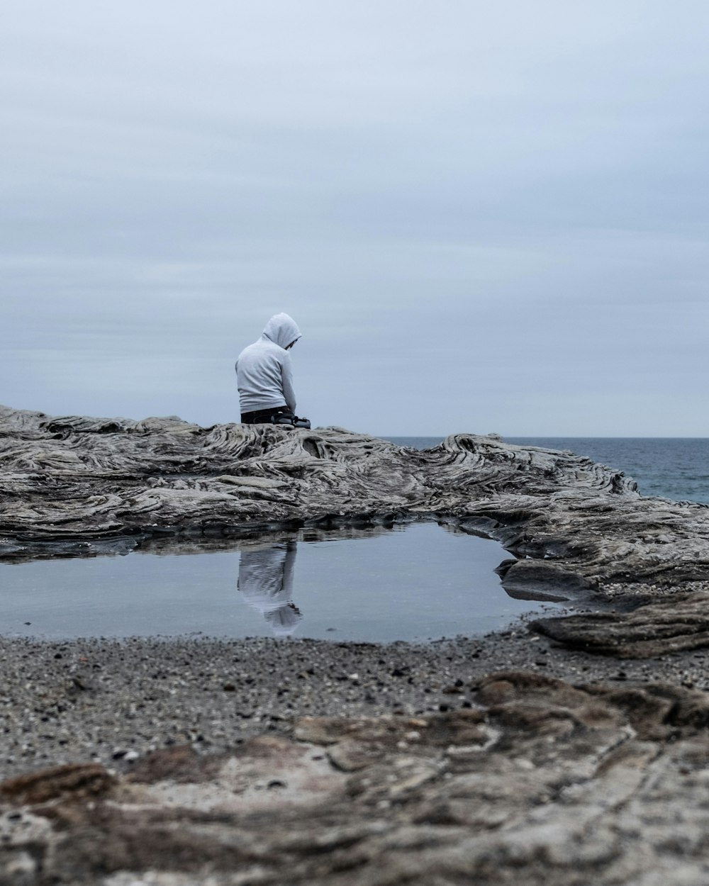 Un hombre sentado en un acantilado con vistas a un mar sombrío