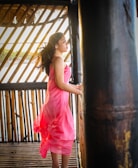 Model wearing a chic, flowing dress in soft pink tones standing in a sunlit, airy room.