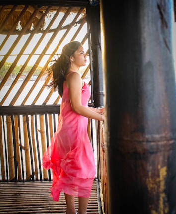 Model wearing a chic, flowing dress in soft pink tones standing in a sunlit, airy room.