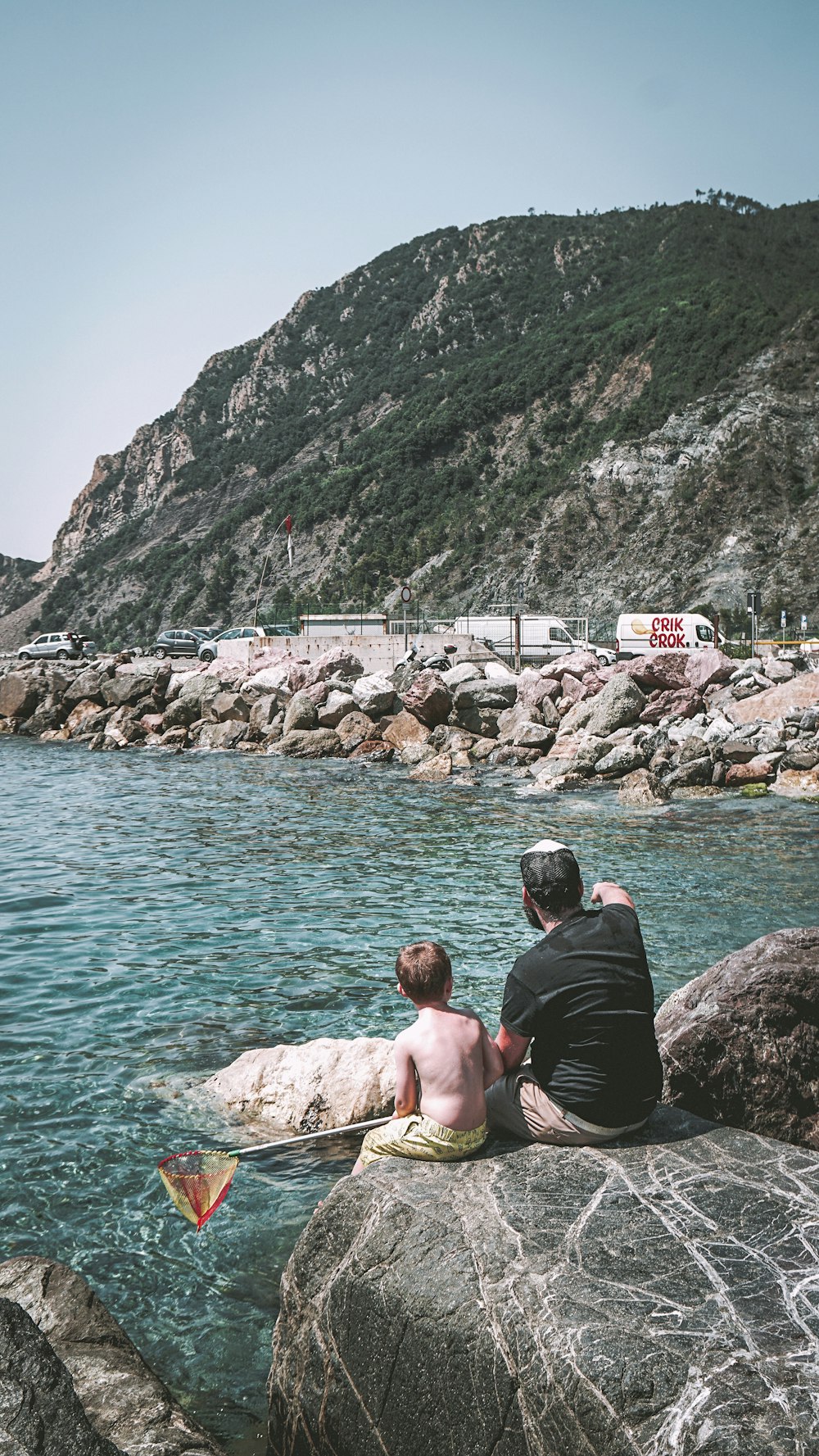 man and boy sitting on rock formation infront of water