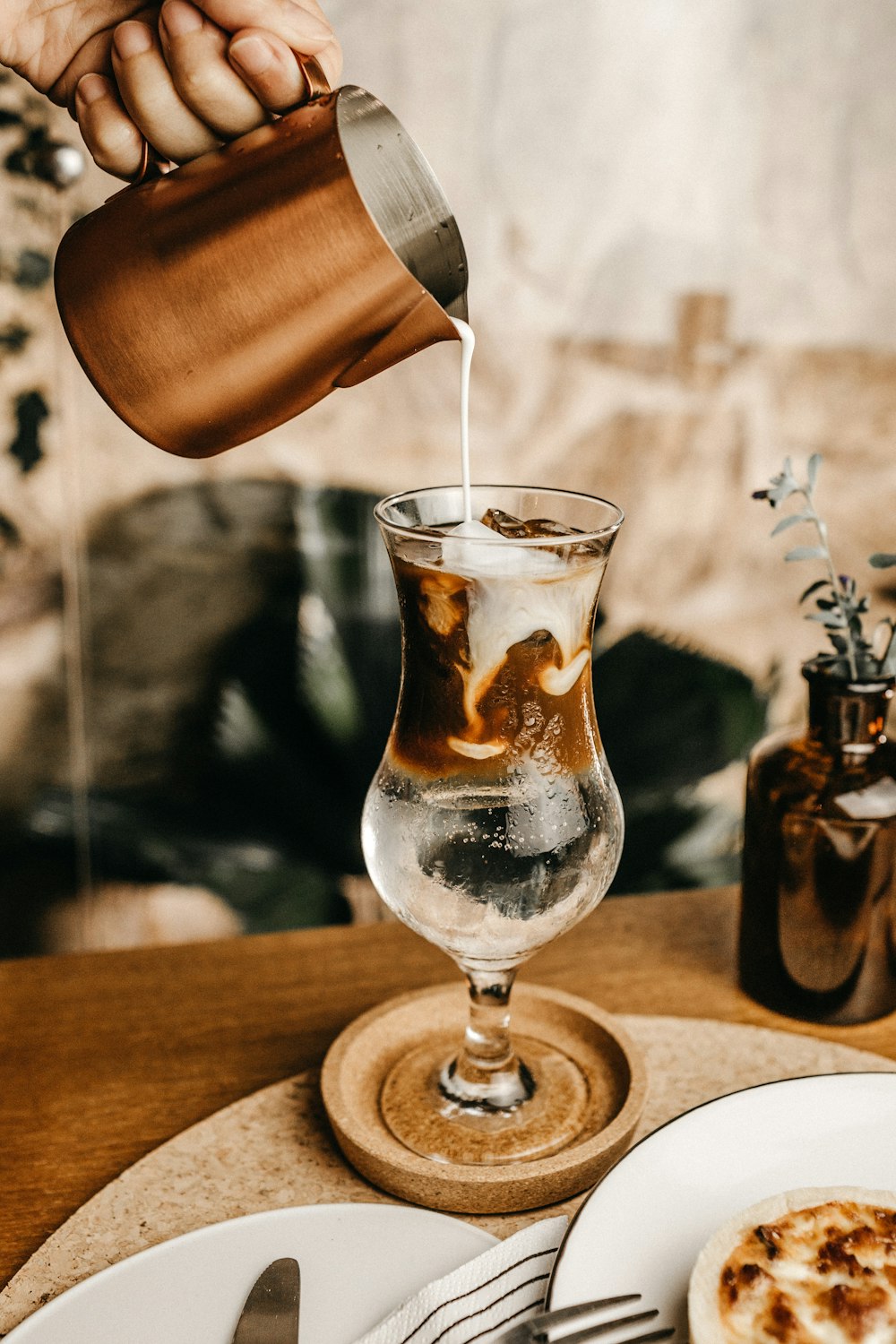 person pouring milk on clear footed drinking glass