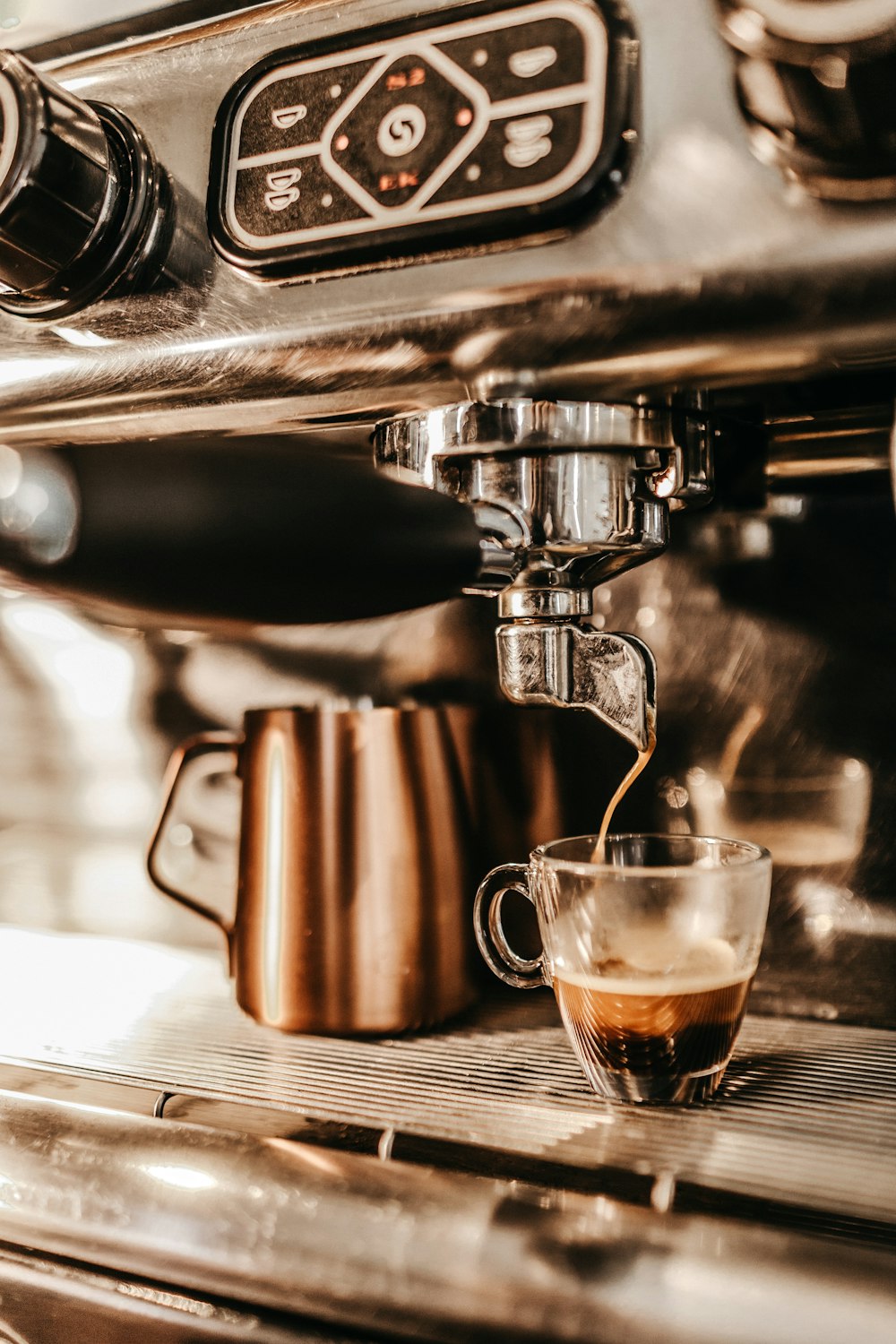 grey industrial coffee maker pouring espresso in clear glass cup