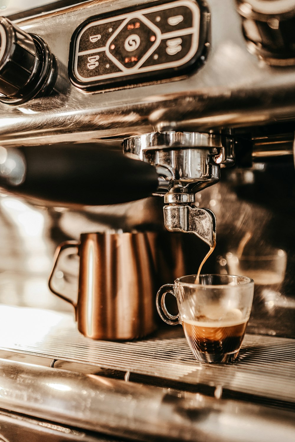 Graue industrielle Kaffeemaschine, die Espresso in eine klare Glastasse gießt