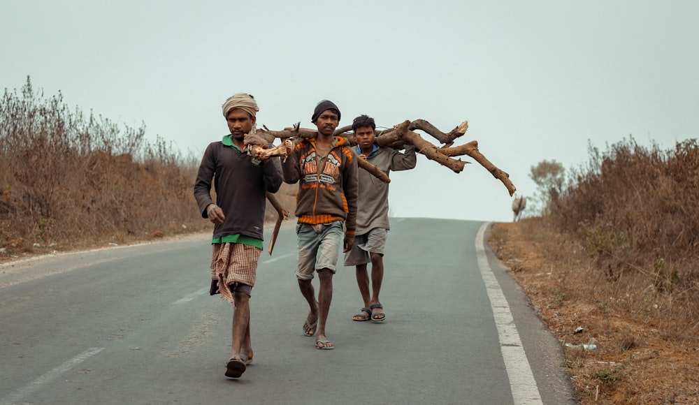 three man walking on the street carrying tree log