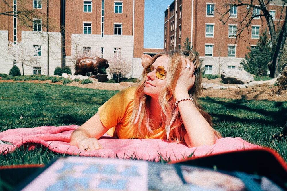 woman lying on pink blanket in grassfield near building