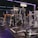 A gym equipped with various weightlifting machines, benches, and barbells. The environment is dimly lit with neon purple lights accentuating the modern gym interior.