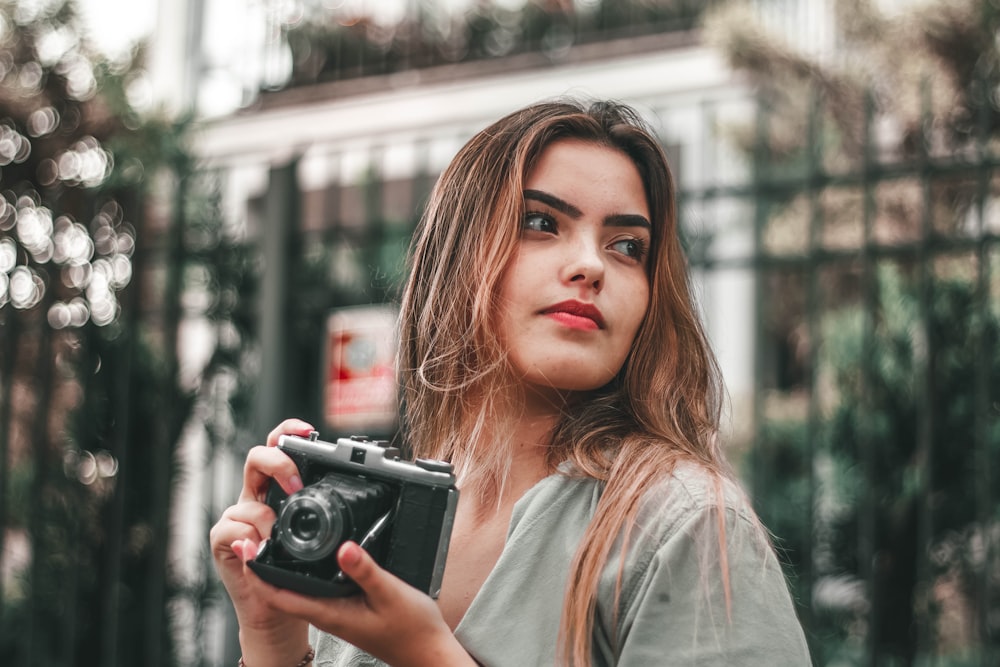 selective focus photography of woman wearing gray top holding camera