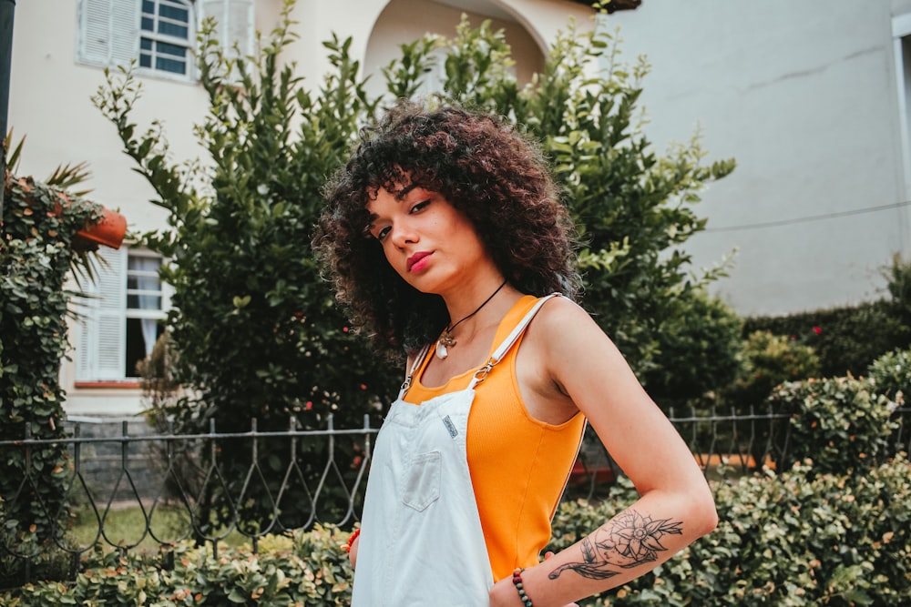 woman in orange spaghetti strap top and white overalls stading near metal fence