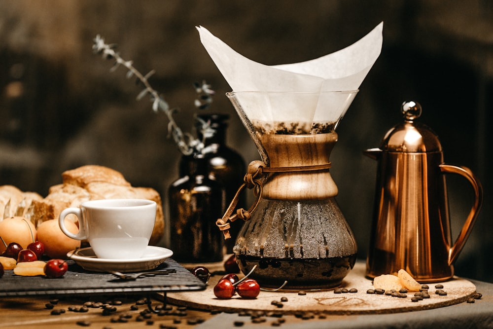 white ceramic teacup beside breads and coffee pot