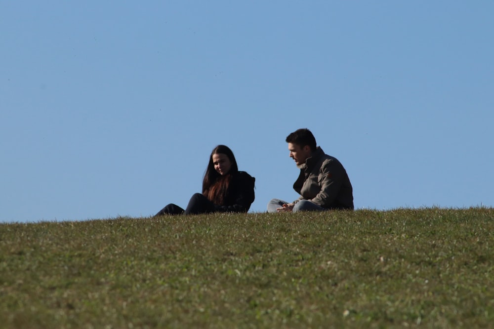 uomo e donna che si siedono sul campo di erba verde durante il giorno