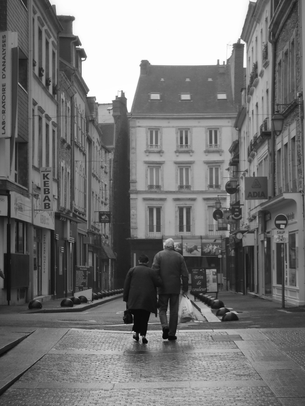 grayscale photo of man and woman walking towards building