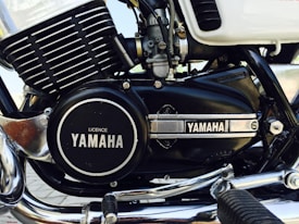 A close-up image of a motorcycle engine featuring the Yamaha branding prominently displayed on the engine casing. The engine has a combination of black and chrome elements, with visible components such as fins, bolts, and a foot peg. The overall appearance is clean and well-maintained, highlighting details of the engine's structure.