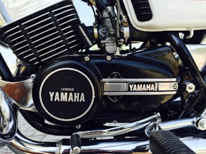 A close-up image of a motorcycle engine featuring the Yamaha branding prominently displayed on the engine casing. The engine has a combination of black and chrome elements, with visible components such as fins, bolts, and a foot peg. The overall appearance is clean and well-maintained, highlighting details of the engine's structure.