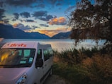 Katie and Dan parked beside a serene lake in their camper van during a Canadian sunset.