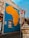 A large mural of Africa painted on a building wall with bright yellow and blue colors. Nearby, there is a 'No Entry' road sign and a 'One Way' sign attached to the wall. The surrounding area has urban elements such as a street lamp and textured walls.