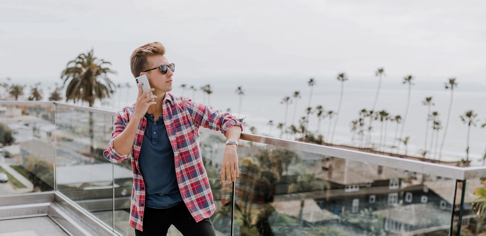 Hombre con camisa roja a cuadros hablando por teléfono en la terraza