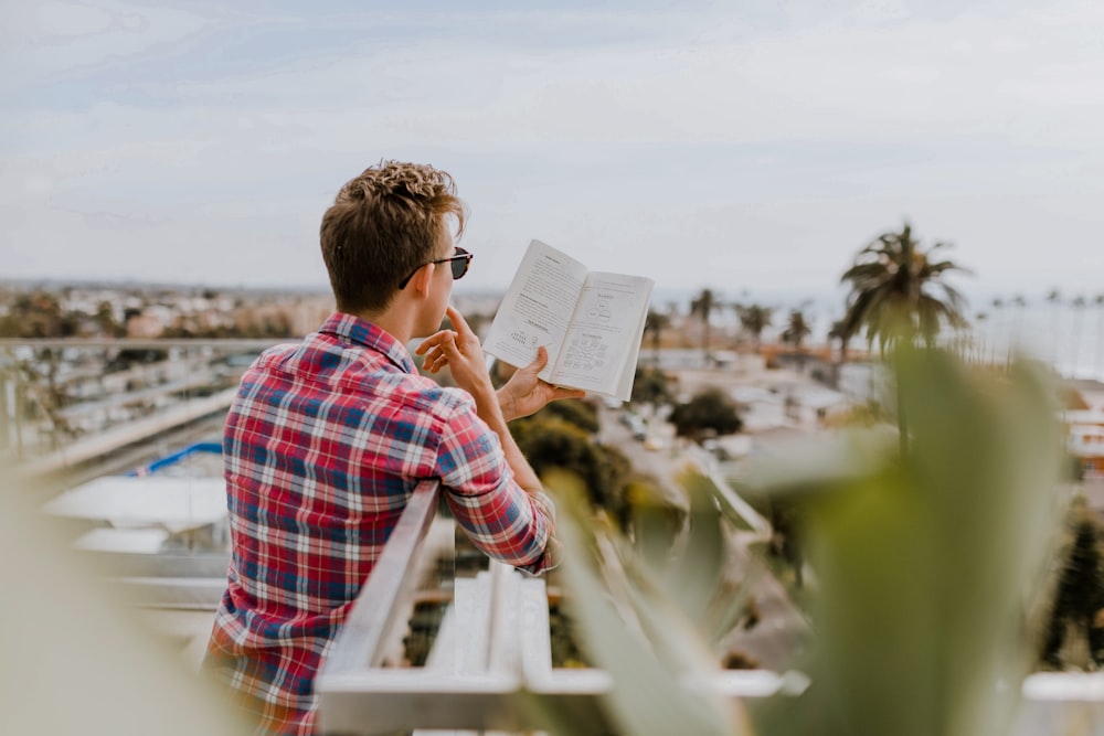 homme lisant un livre sur le balcon pendant la journée