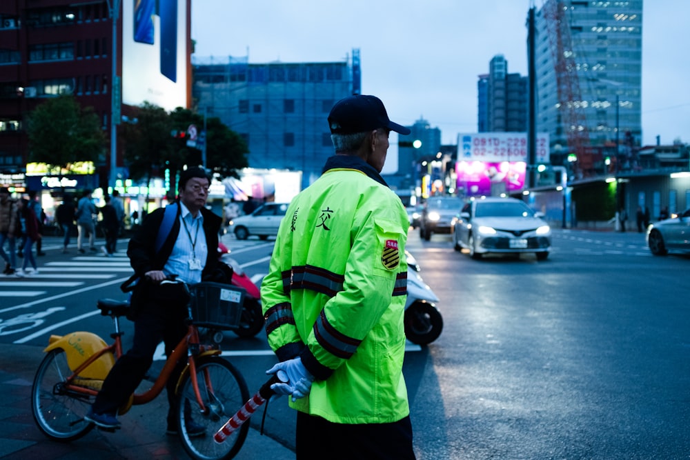 man in green and black jacket standing beside road