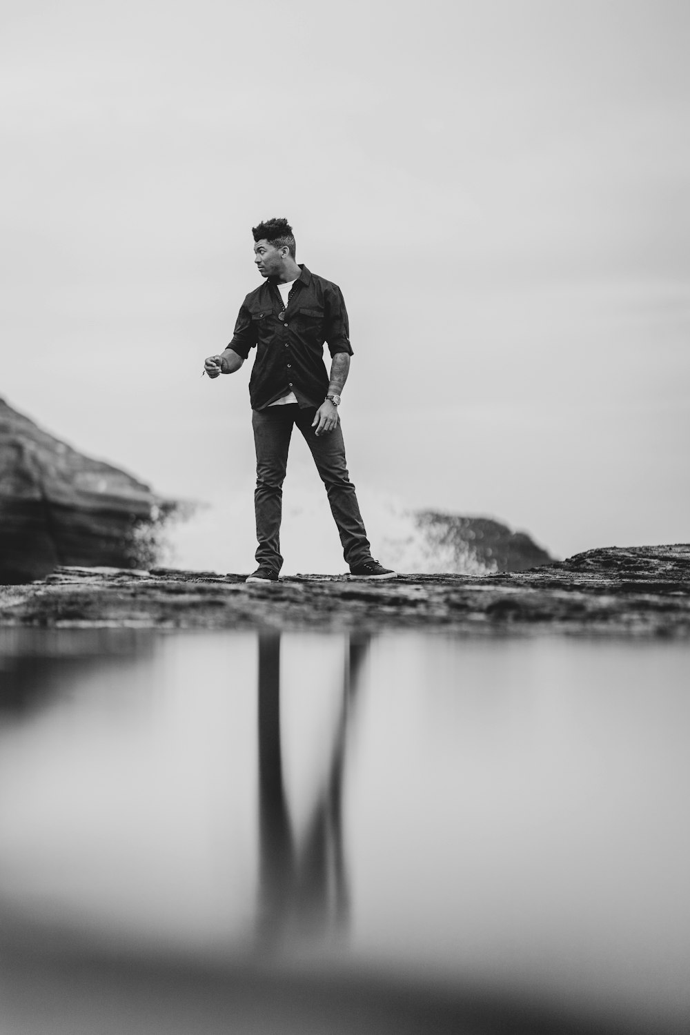 grayscale photo of man standing beside water