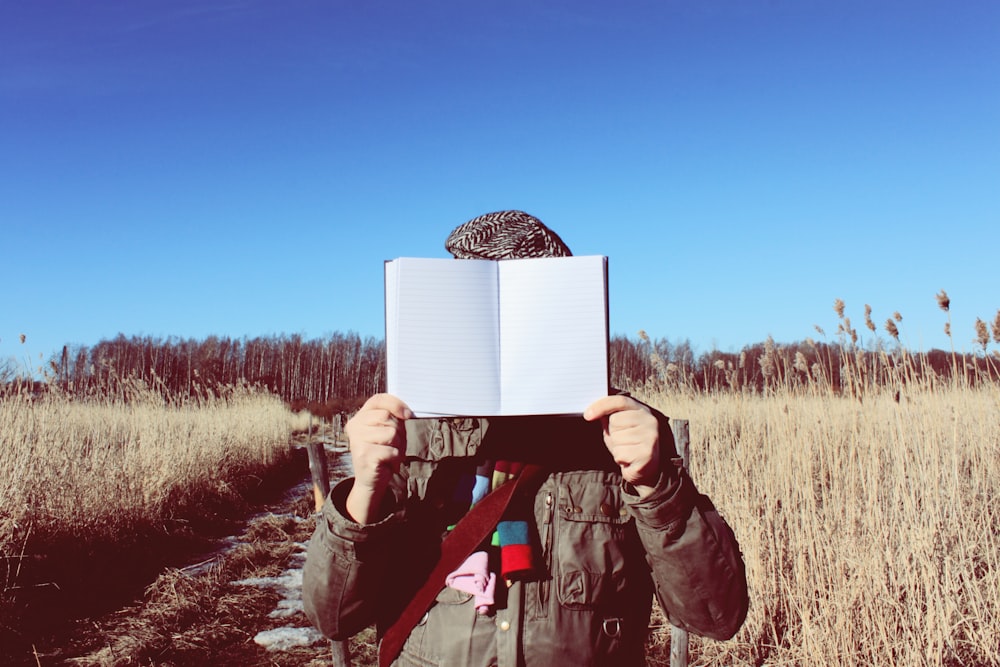 person holding book while standing on field during daytime