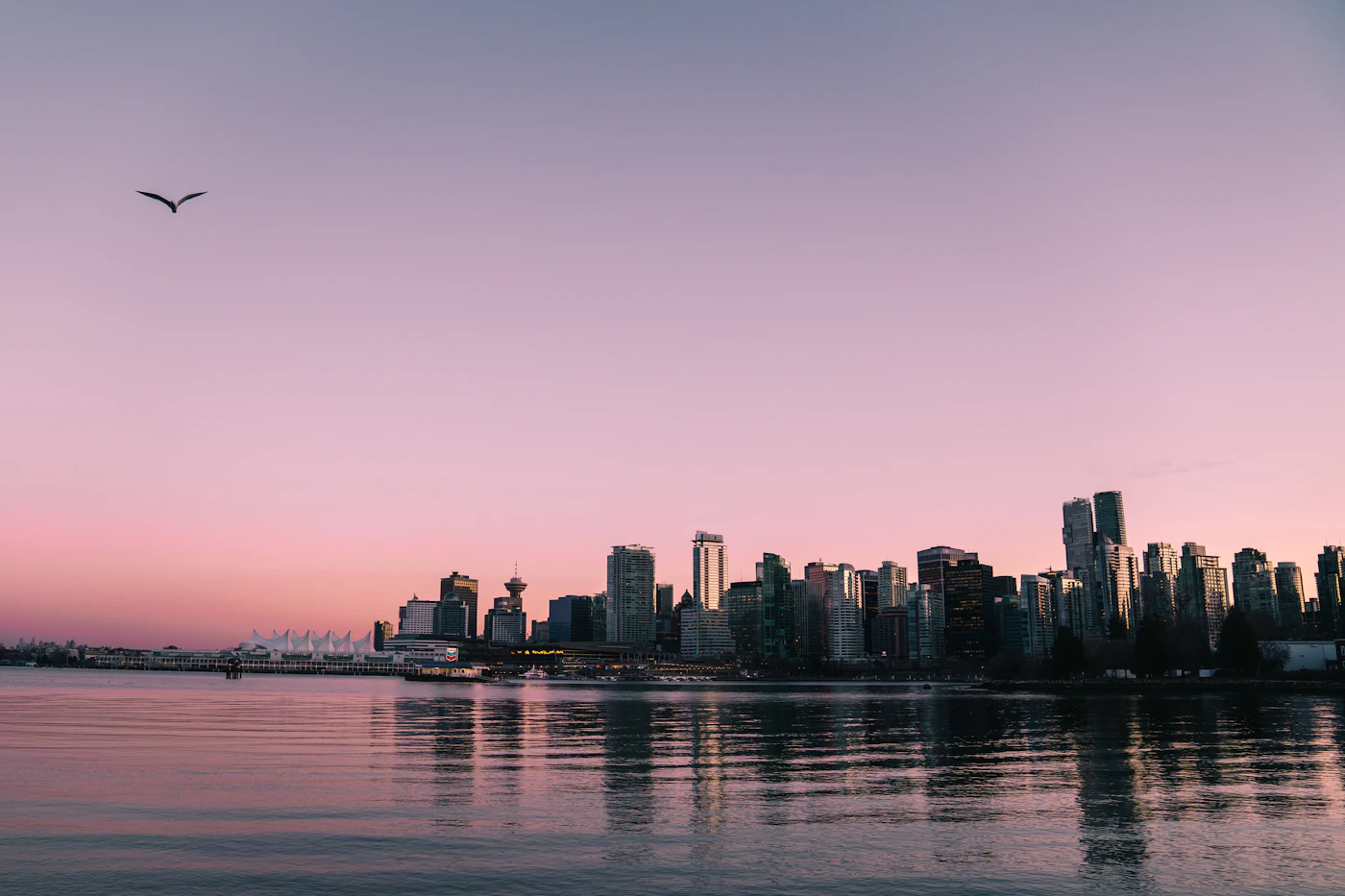 Vancouver at sunset with the downtown skyline glowing in golden light over the water and the coastal mountains in the distance