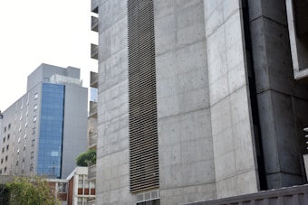 Large modern buildings with concrete facades and glass windows, featuring a minimalist architectural design. The structures appear to be part of an urban environment.