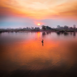 A fisherman casting nets into a calm river at sunrise.