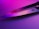 A sharp knife blade reflecting pink and purple lighting, creating a vibrant and modern aesthetic. The metal surface shows a logo engraved near the handle.