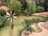 A small pond is surrounded by lush green vegetation and two colorful windmills. Steps made of brick lead down to a landscaped area near the pond. Various shades of green foliage provide a backdrop, creating a serene and natural setting.