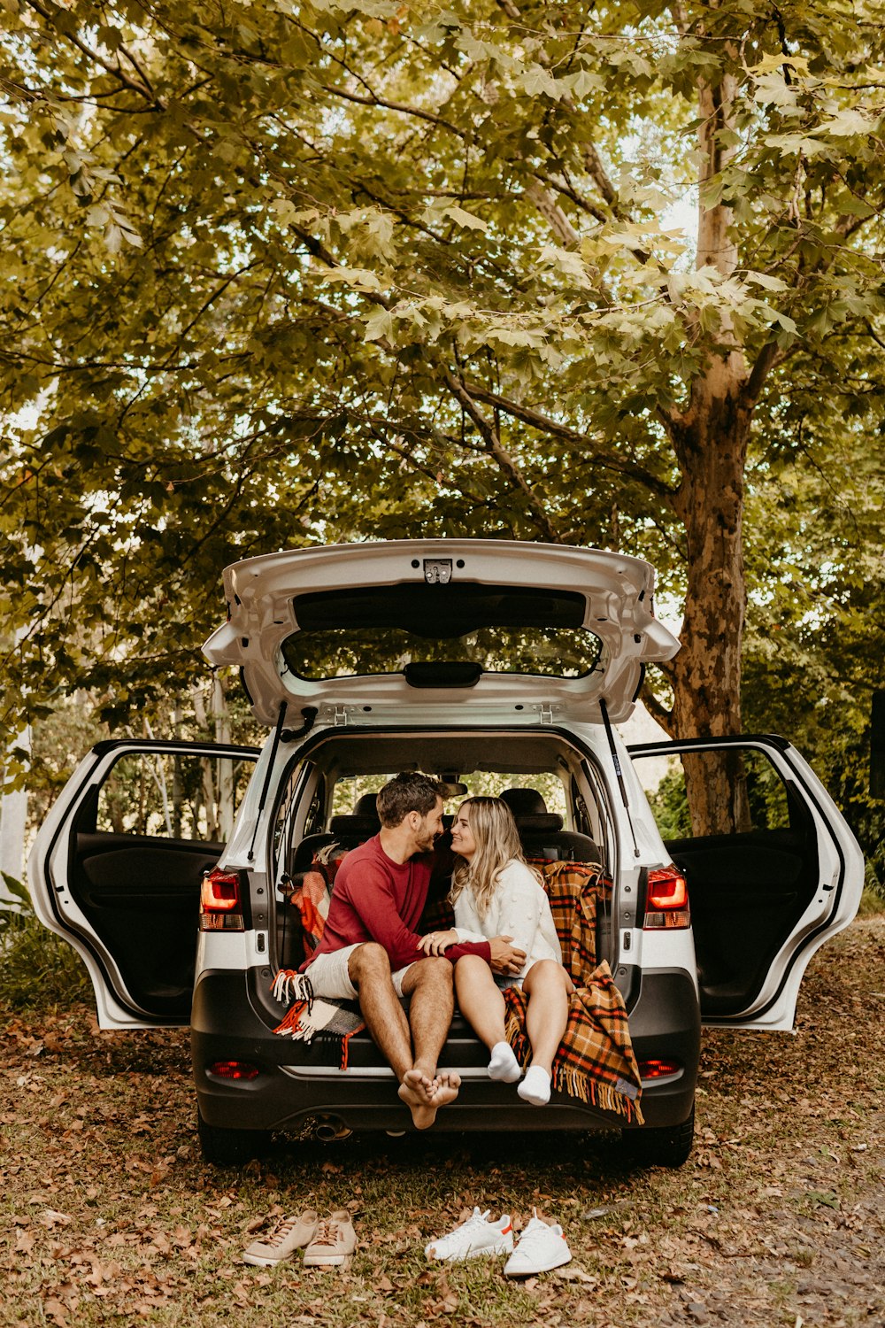 man sitting near woman smiling while facing each other at the back of open vehicle beside trees