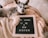A small dog is lying comfortably on beige blankets, next to a letter board. The board displays the message, 'I'M GOING TO BE A BIG SISTER,' indicating a playful or affectionate announcement likely related to a family expecting a child.