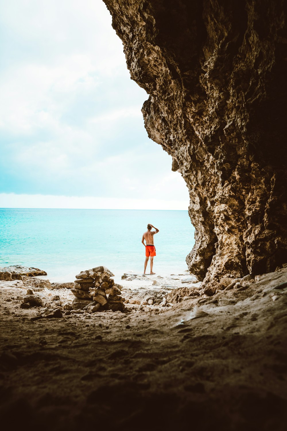 person standing beside rock formation near body of water during daytime