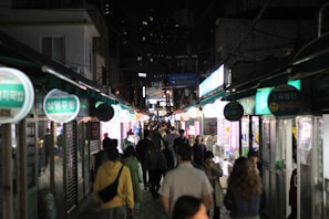 A lively street scene with people walking under bright city lights at night