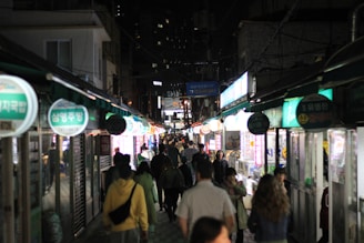 A lively street scene with people walking under bright city lights at night