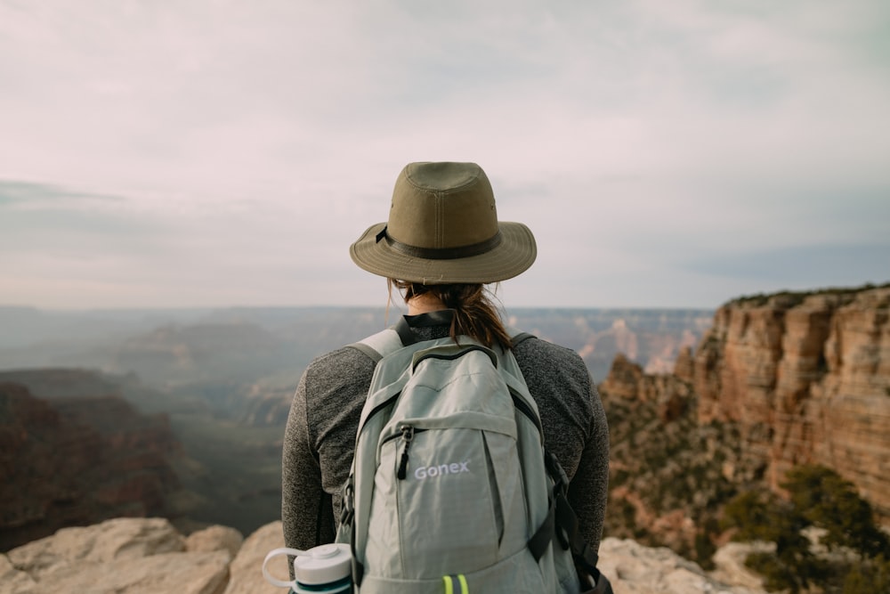 Persona con sombrero gris de pie en el acantilado de la montaña