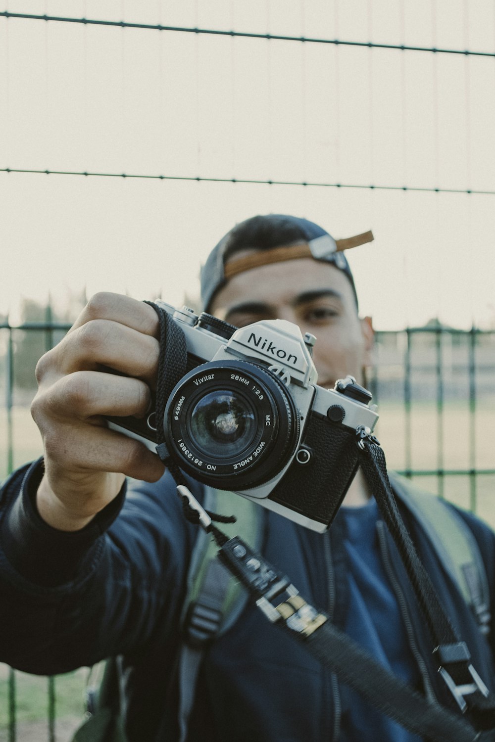 hombre sosteniendo una cámara DSLR Nikon en blanco y negro al aire libre durante el día