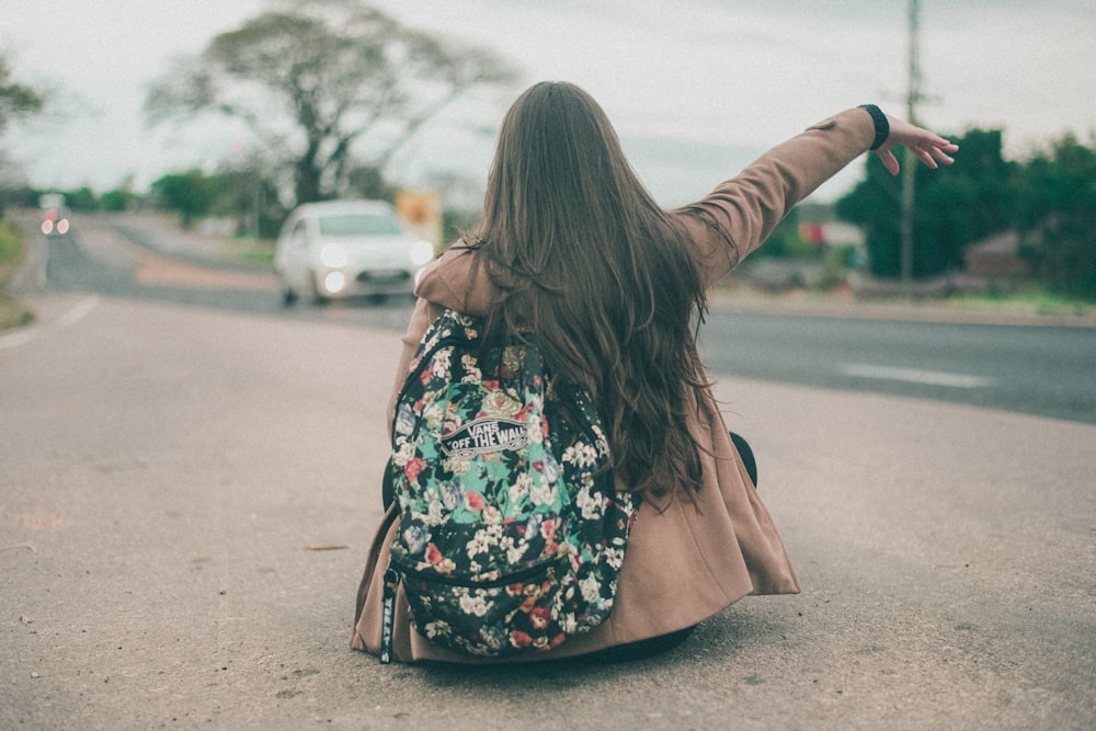 woman sitting and raising right hand on concrete pathway near road