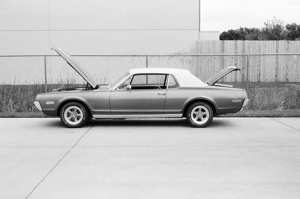 grayscale photo of coupe parked near fence