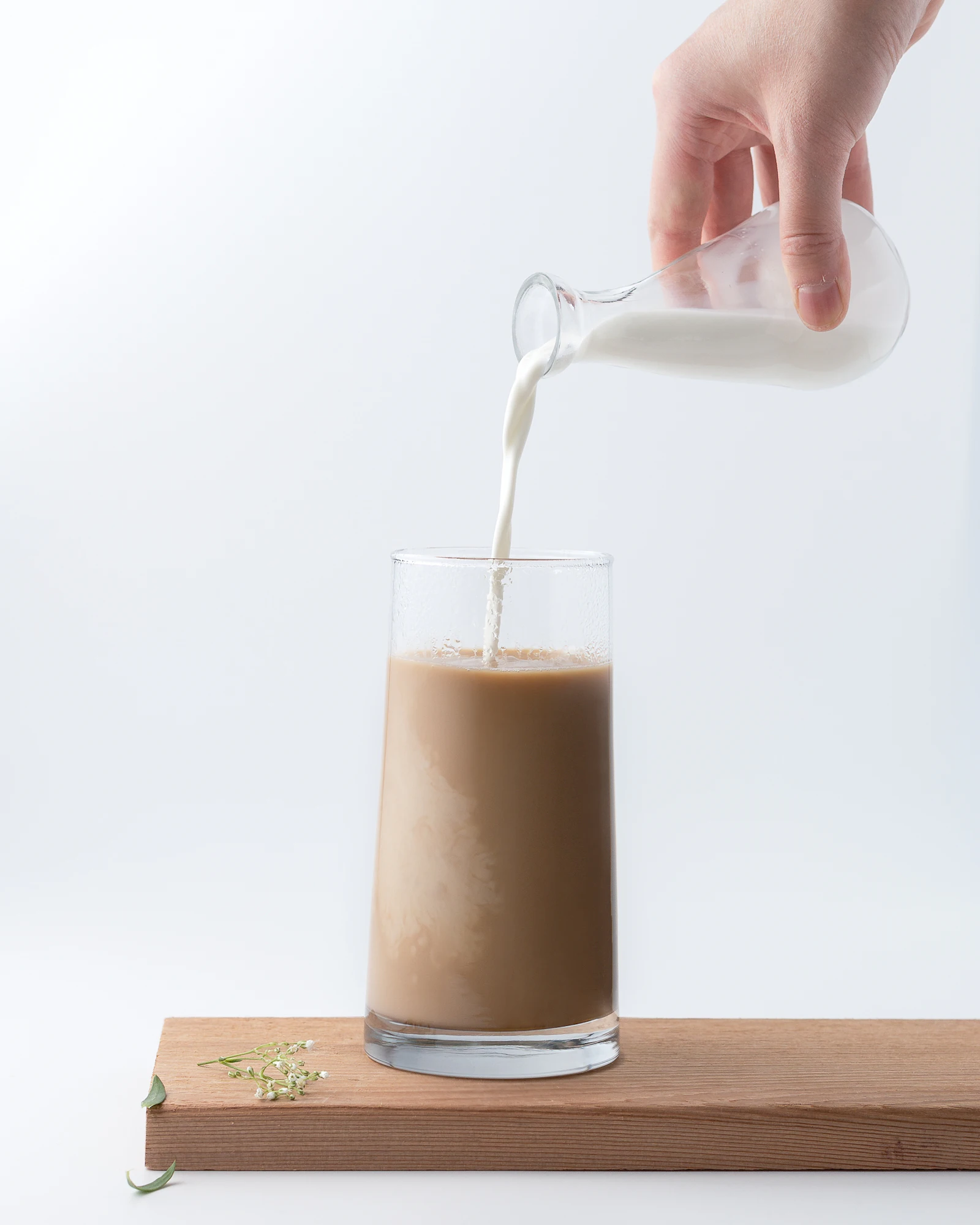 Milk being poured into a glass of tea on a wooden board