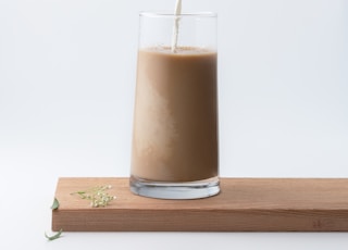 person pouring milk into chocolate filled glass cup