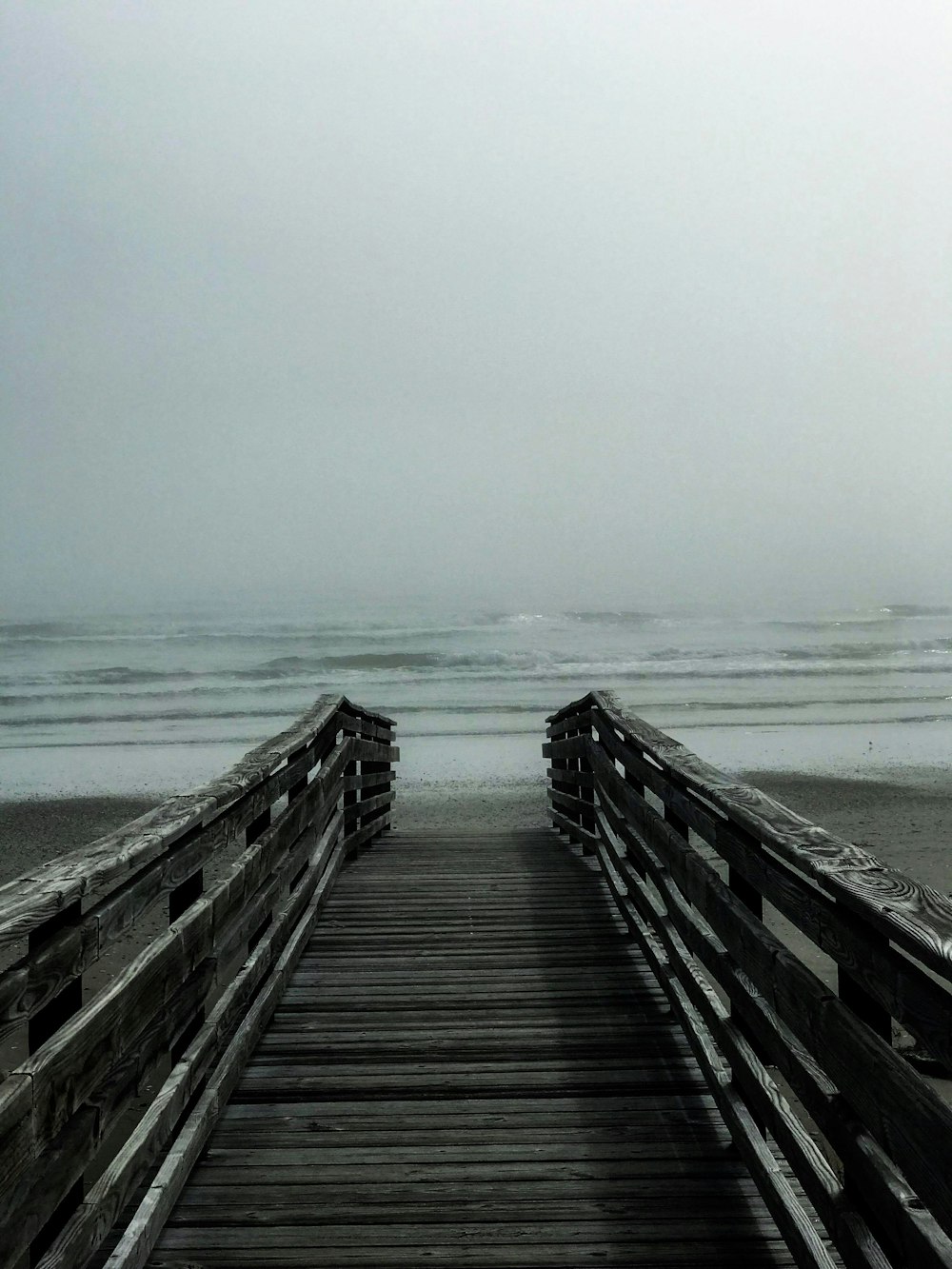 grayscale photo of footbridge through the sea